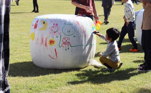 ロールベール（牧草をラップで巻いたもの）にペンでお絵描きする男の子の写真